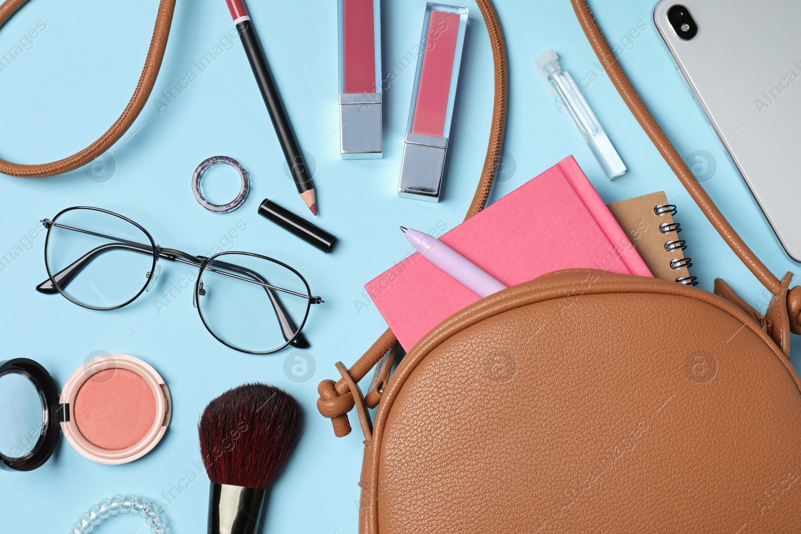 Photo of Stylish woman's bag with smartphone and accessories on light blue background, flat lay