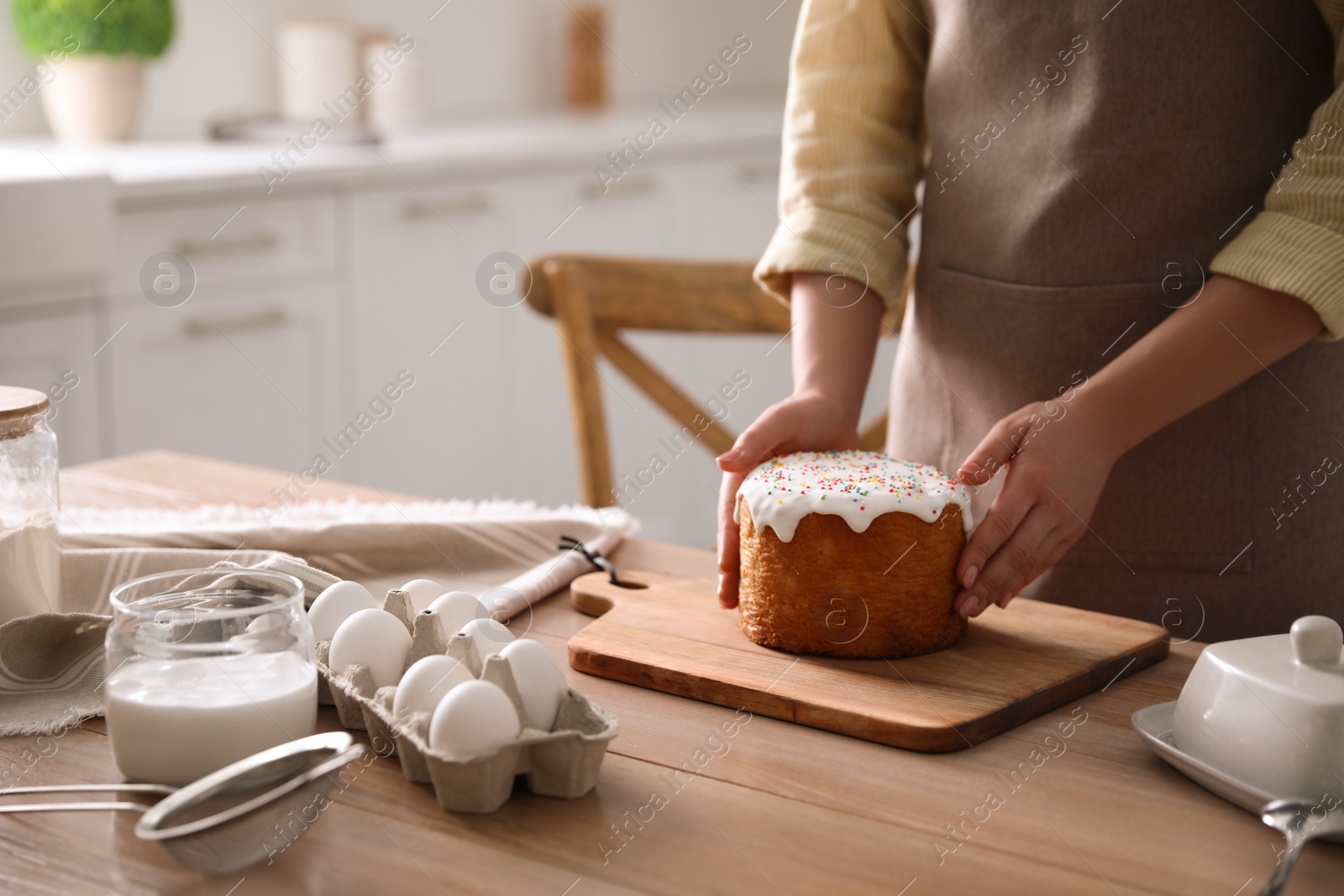 Photo of Young woman with traditional Easter cake at table in kitchen, closeup