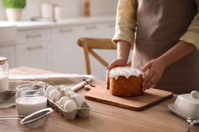 Photo of Young woman with traditional Easter cake at table in kitchen, closeup