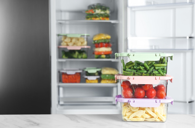 Photo of Containers with different frozen vegetables on white marble table near open refrigerator