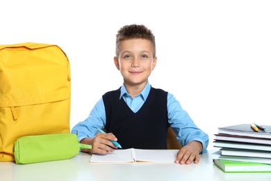 Photo of Little boy in uniform doing assignment at desk against white background. School stationery