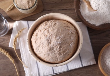 Photo of Fresh sourdough in proofing basket, flour and spikes on wooden table, flat lay