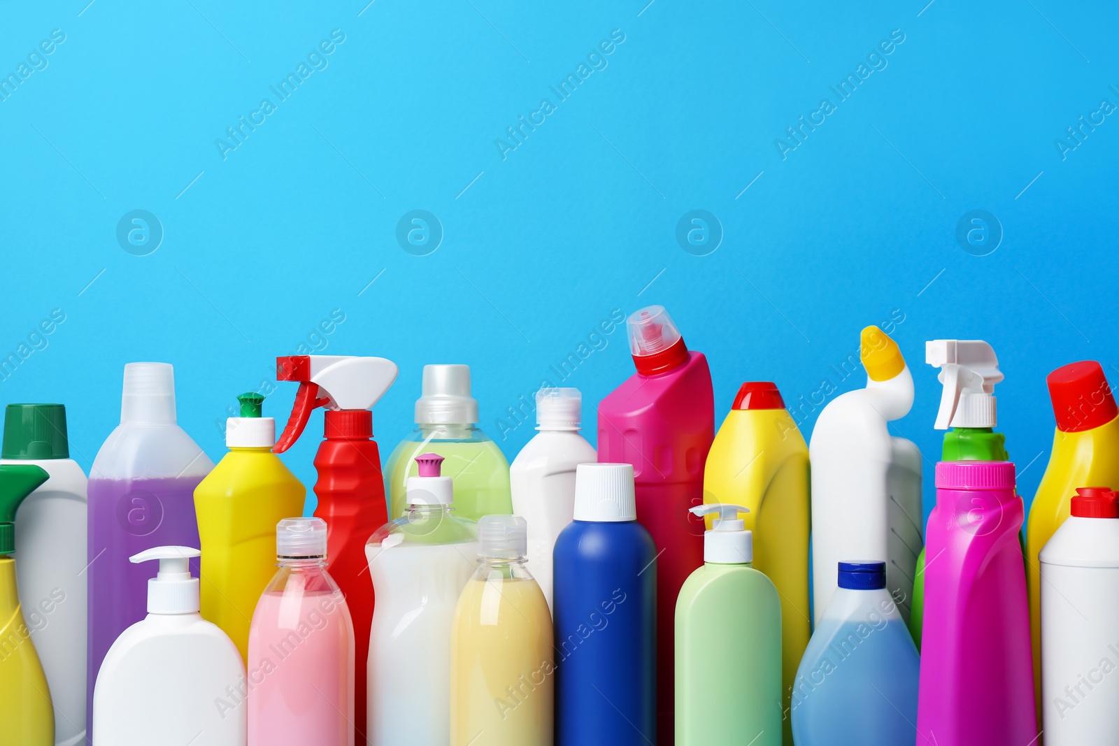 Photo of Many bottles of different detergents on light blue background. Cleaning supplies