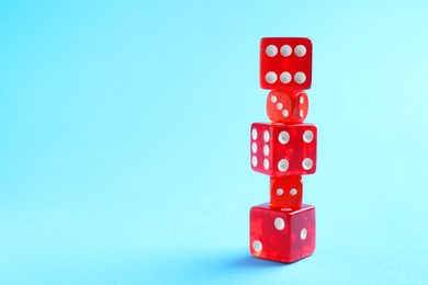 Photo of Many stacked red game dices on light blue background, closeup. Space for text