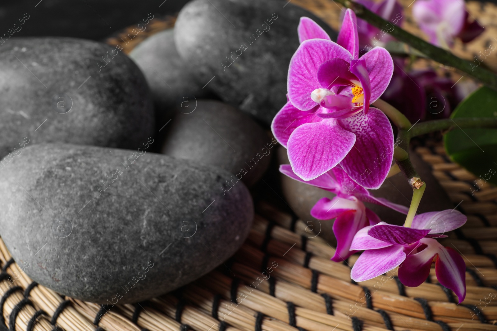 Photo of Composition with orchid flowers and spa stones on wicker mat