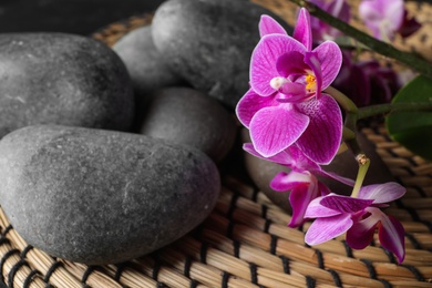 Photo of Composition with orchid flowers and spa stones on wicker mat