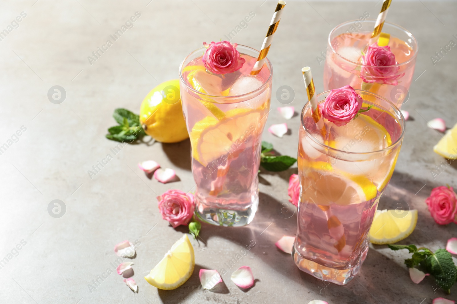 Photo of Delicious refreshing drink with rose flowers and lemon slices on light grey table