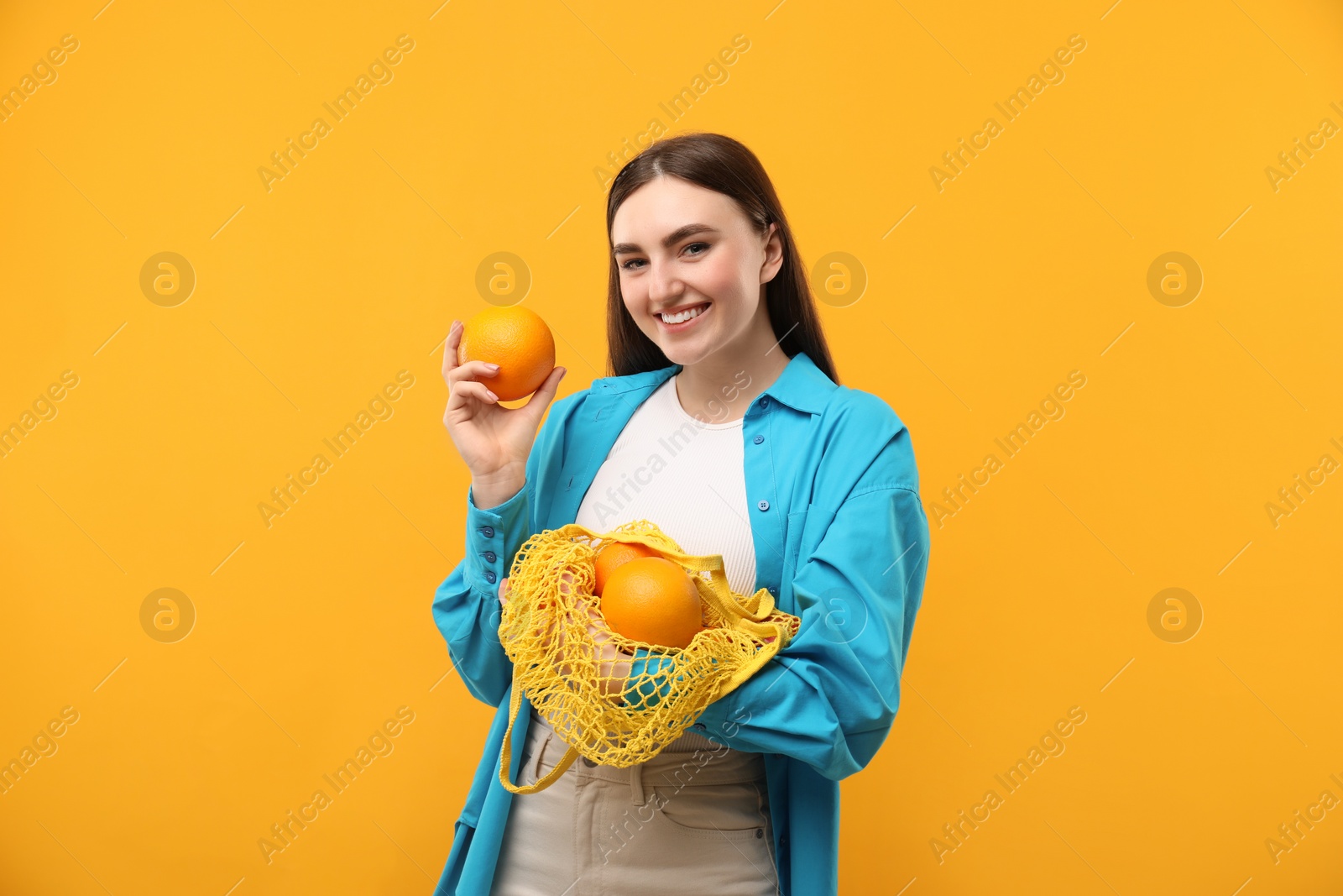 Photo of Woman with string bag of fresh oranges on orange background