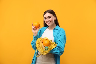 Woman with string bag of fresh oranges on orange background