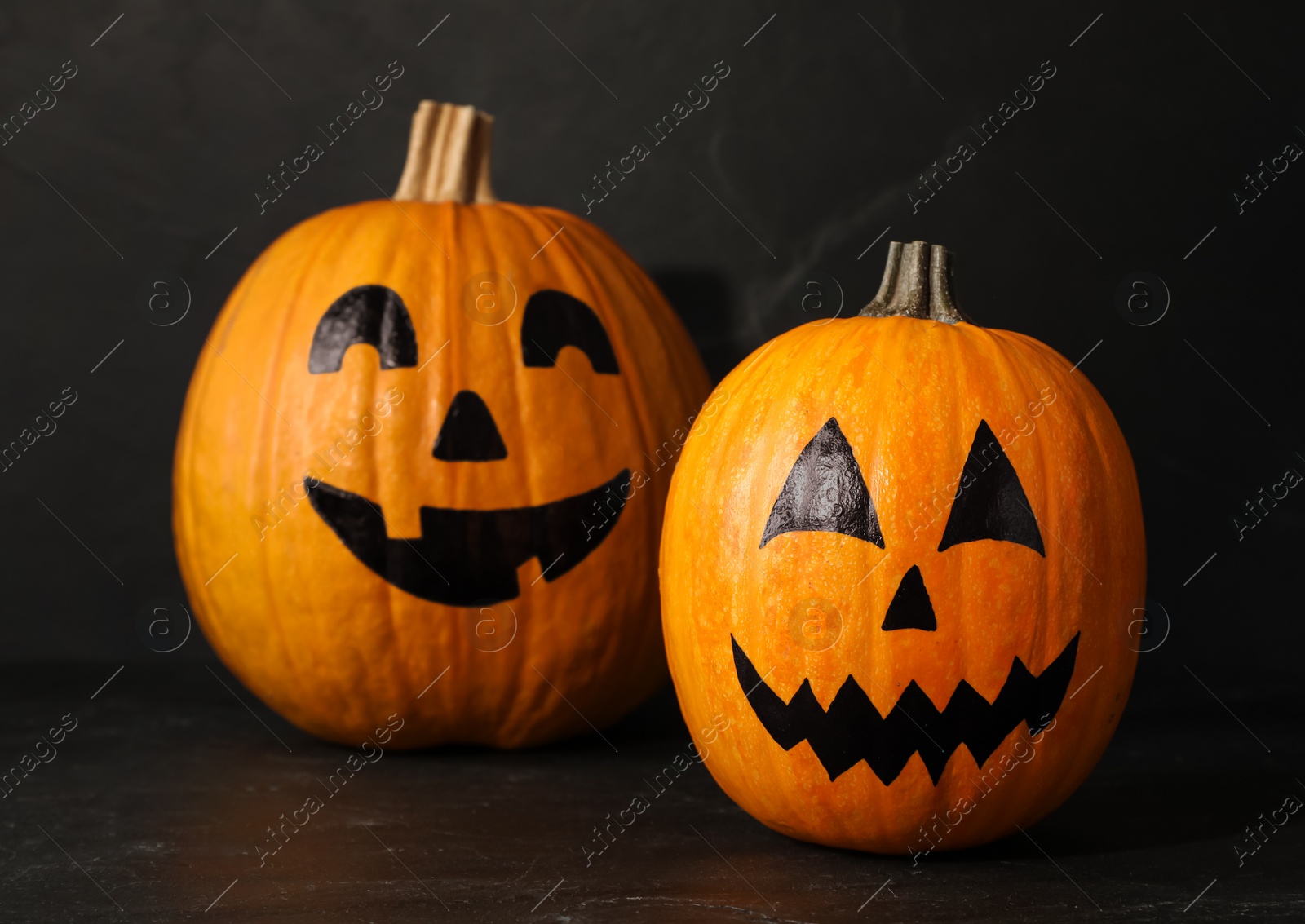 Photo of Pumpkins with drawn spooky faces on dark background. Halloween celebration