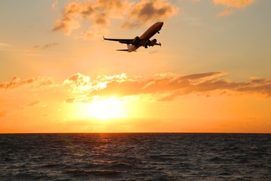 Image of Plane flying over sea during sunset. Sun shining through clouds