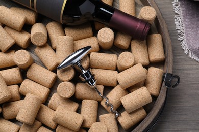 Photo of Corkscrew, wine bottle and stoppers on wooden tray, top view