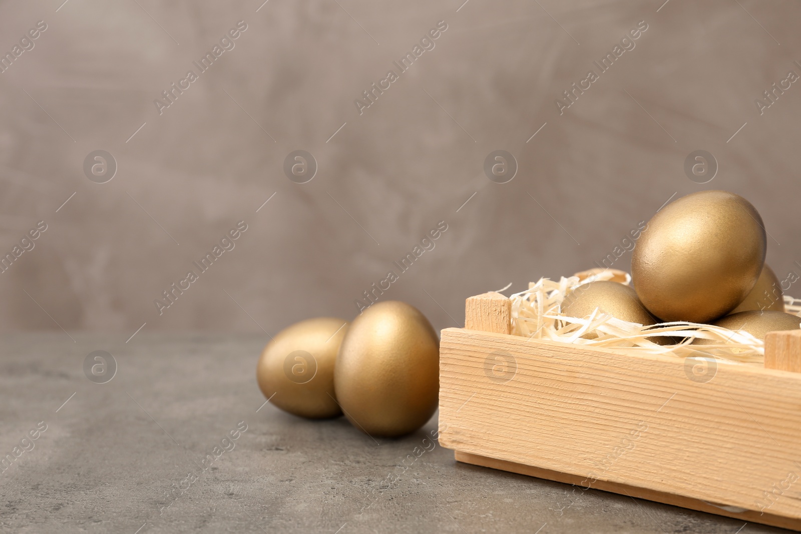 Photo of Wooden crate with golden eggs on table, space for text