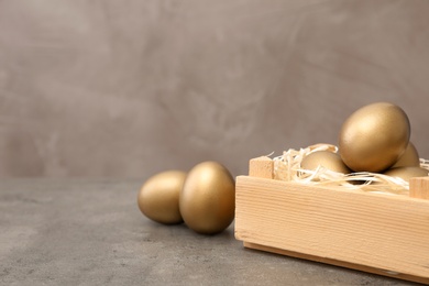 Wooden crate with golden eggs on table, space for text