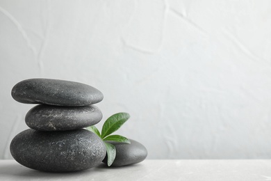 Stack of spa stones and green leaves on grey table, space for text