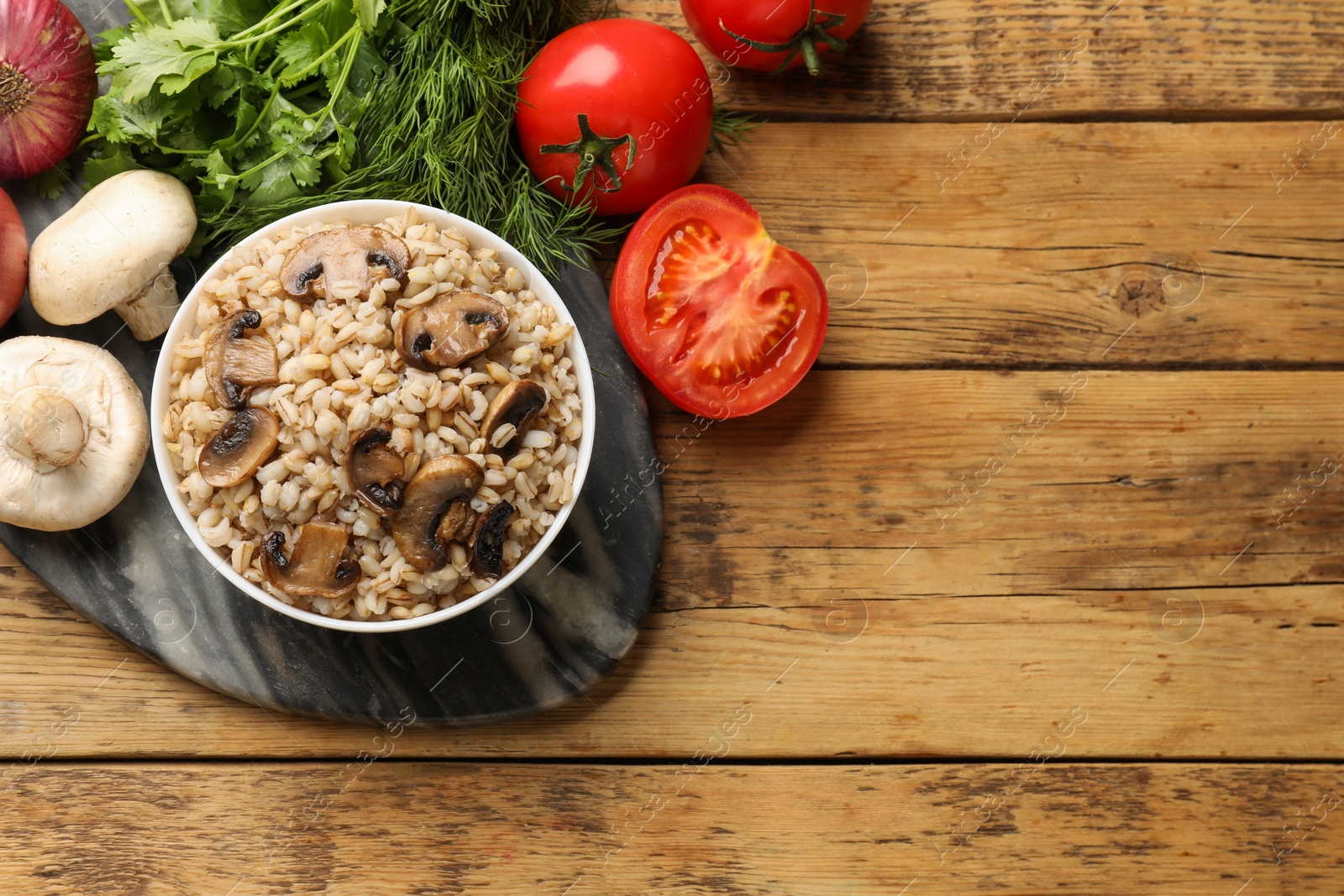 Photo of Delicious pearl barley in bowl served on wooden table, flat lay. Space for text