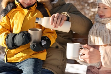 Photo of Happy family warming themselves with hot tea outdoors on sunny winter day, closeup