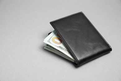 Stylish black leather wallet with dollar banknotes on light grey background. Space for text