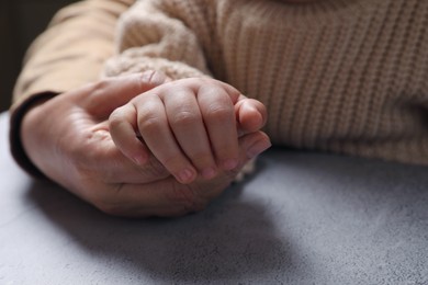 Woman holding hands with her little daughter at light grey table, closeup