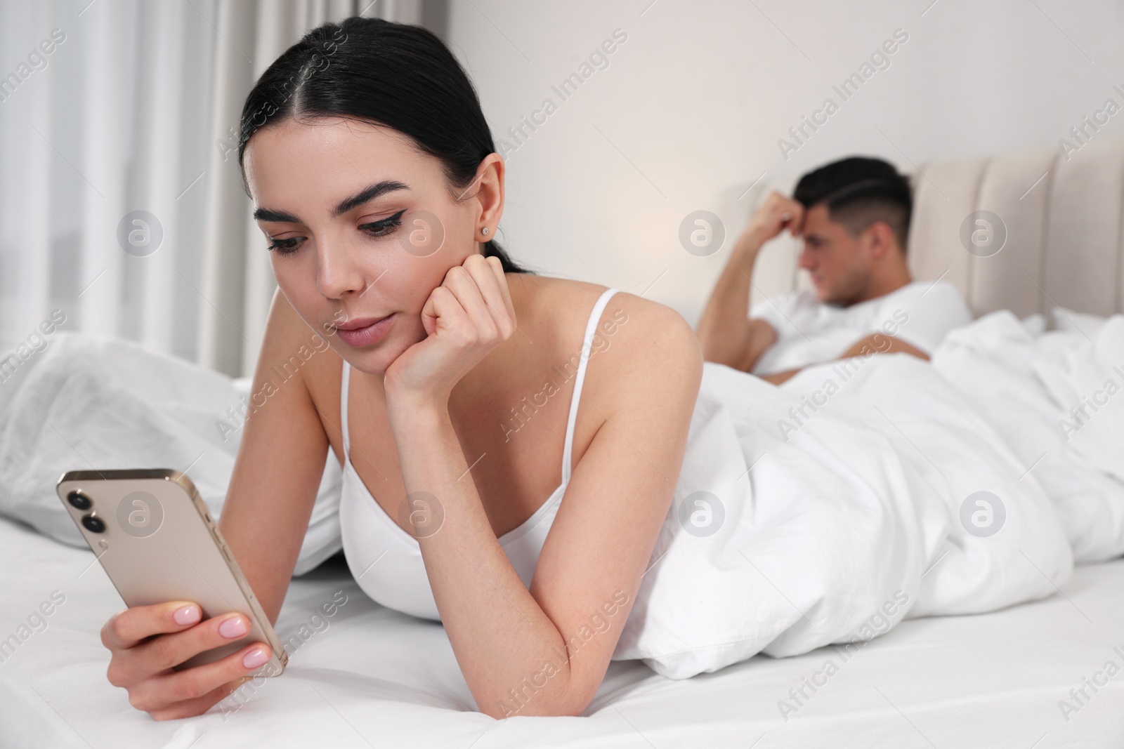 Photo of Internet addiction. Woman with smartphone ignoring her boyfriend in bedroom