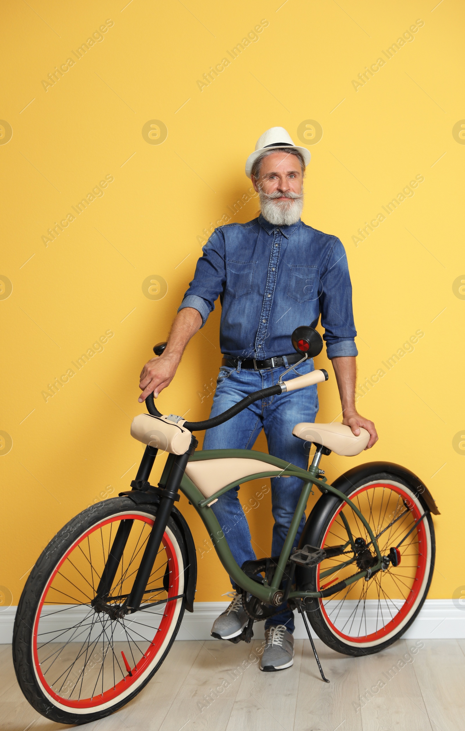 Photo of Portrait of handsome mature man with bicycle near color wall