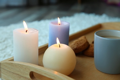 Burning candles and cup of coffee on wooden tray