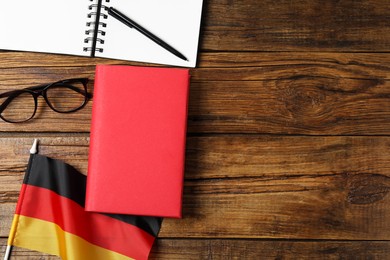 Photo of Learning foreign language. Flag of Germany, book, glasses and stationery on wooden table, flat lay with space for text