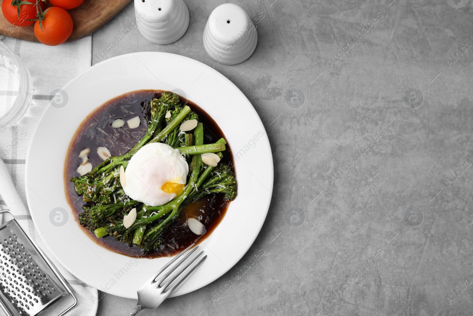 Photo of Tasty cooked broccolini with poached egg, almonds and sauce on grey table, flat lay. Space for text