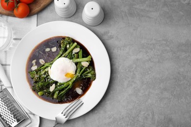 Photo of Tasty cooked broccolini with poached egg, almonds and sauce on grey table, flat lay. Space for text