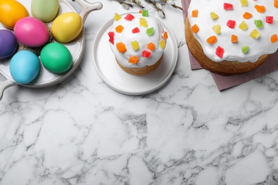 Beautiful Easter cakes and painted eggs on white marble table, flat lay. Space for text