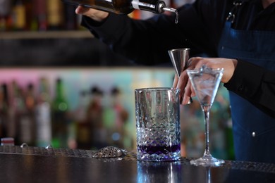 Cocktail making. Bartender pouring alcohol from bottle into jigger at counter in bar, closeup. Space for text