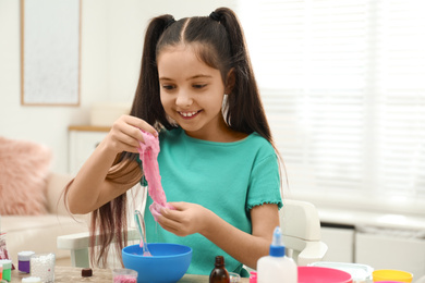 Photo of Cute little girl making DIY slime toy at table indoors