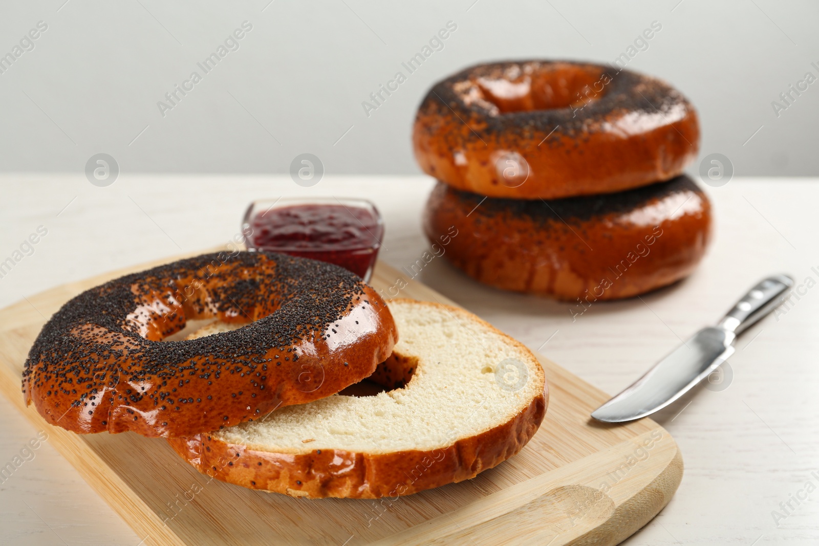 Photo of Delicious fresh bagels with poppy seeds and jam on white wooden table