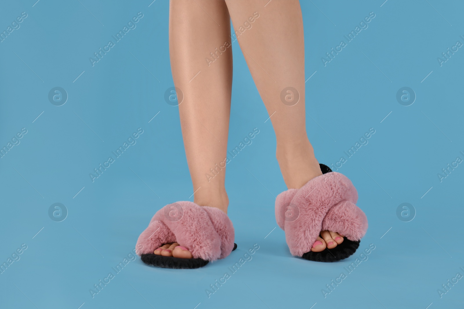 Photo of Woman in fluffy slippers on light blue background, closeup