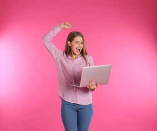 Photo of Emotional young woman with laptop celebrating victory on color background