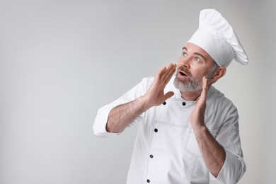 Photo of Surprised chef in uniform on grey background, space for text