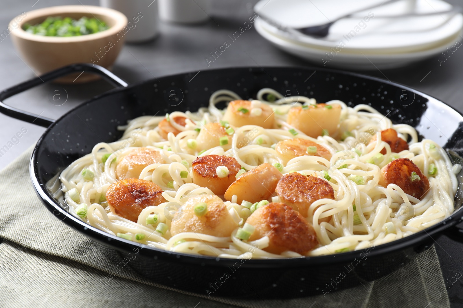 Photo of Delicious scallop pasta with green onion served on grey table, closeup