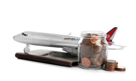 Photo of Airplane model, passport and jar with coins on white background. Money saving concept
