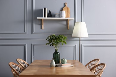 Photo of Vase with green branches, books and decor on wooden table in stylish dining room