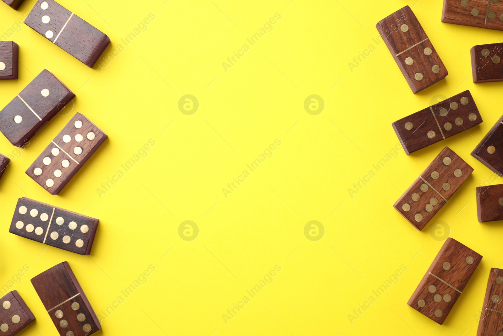 Photo of Wooden domino tiles on yellow background, flat lay. Space for text