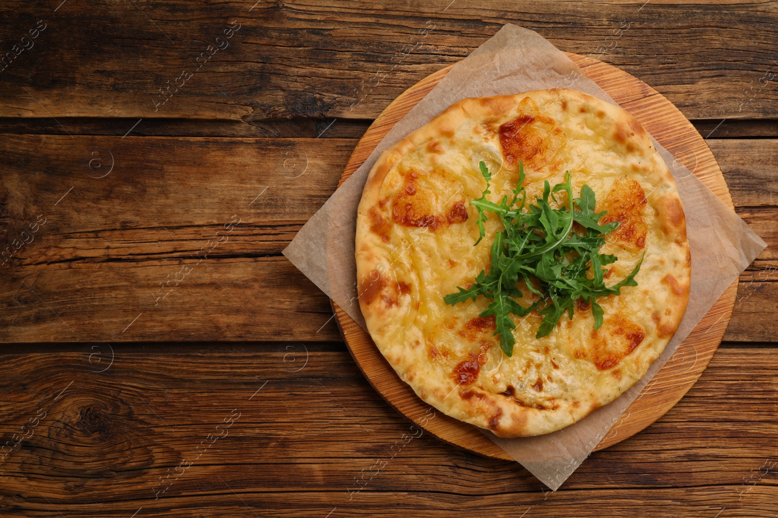 Photo of Delicious khachapuri with cheese and arugula on wooden table, top view. Space for text