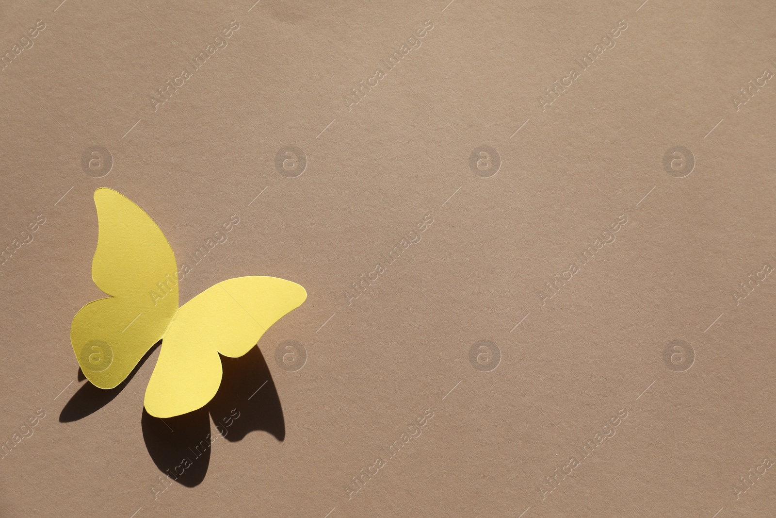 Photo of Yellow paper butterfly on light brown background, top view. Space for text