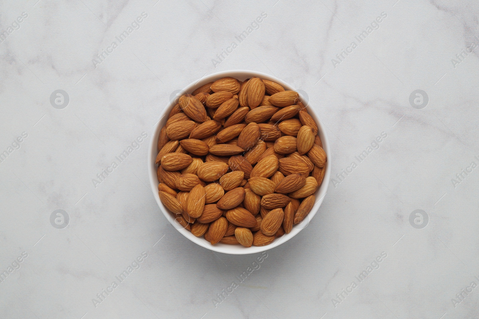 Photo of Bowl of delicious almonds on white marble table, top view