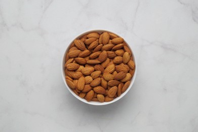 Photo of Bowl of delicious almonds on white marble table, top view