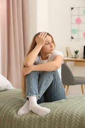 Photo of Upset teenage girl sitting on bed at home