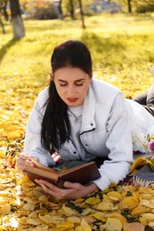 Woman reading book in park on autumn day