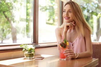 Photo of Young woman with glass of tasty natural lemonade in cafe. Detox drink