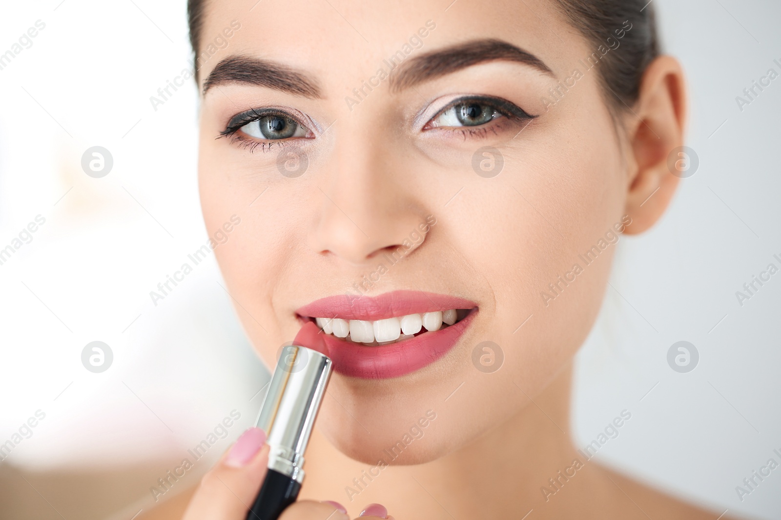 Photo of Young woman applying lipstick on blurred background