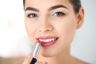 Young woman applying lipstick on blurred background