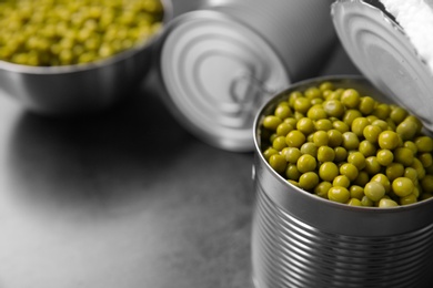 Photo of Open tin can with green peas on grey table, closeup. Space for text